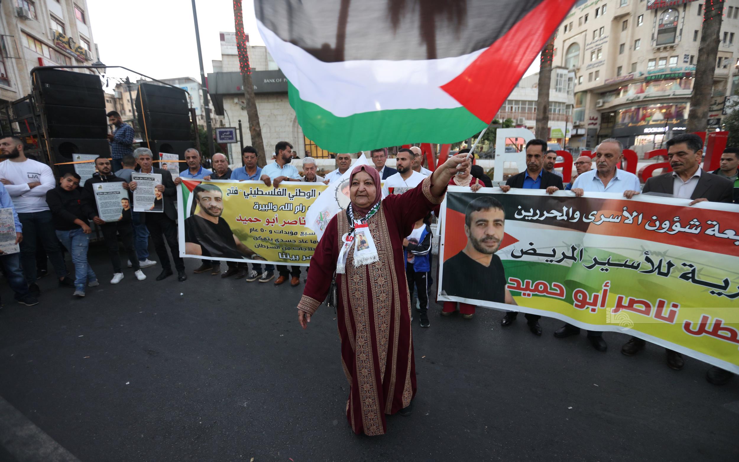 والدة الأسير المريض ناصر أبو حميد تلوّح بالعلم الفلسطيني خلال المسيرة (تصوير: حمزة شلش/وفا)