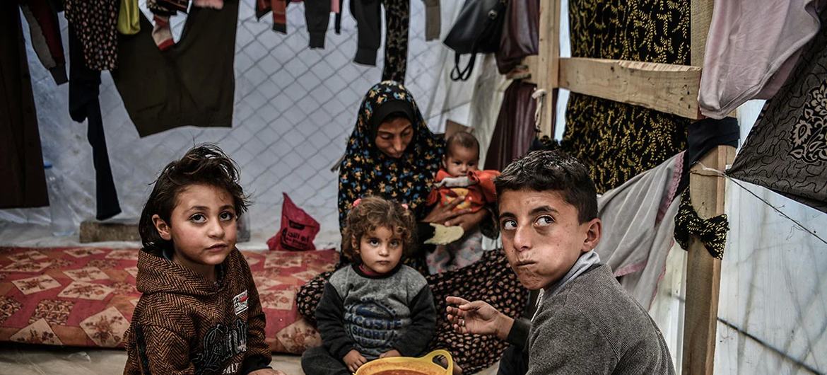 أسرة تجتمع حول وعاء واحد من البقوليات في خيمتها برفح جنوب قطاع غزة (اليونيسف)